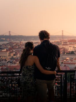 Couple enjoying a romantic sunset view overlooking Lisbon with the iconic 25 de Abril Bridge in the background.